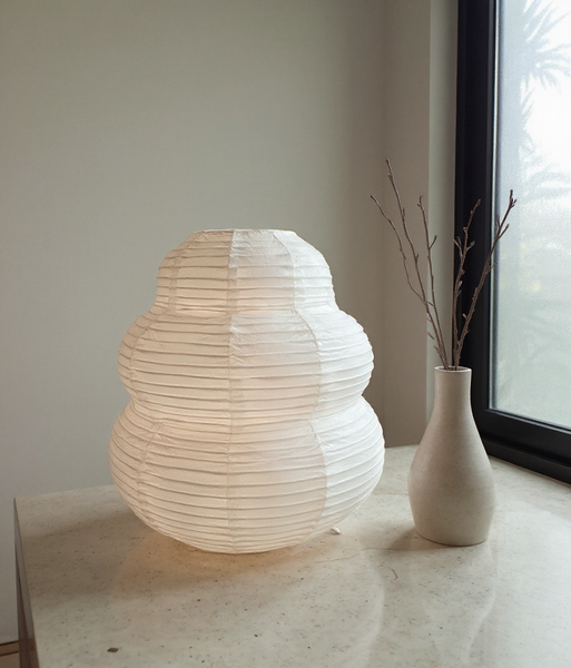 White paper lantern on a surface next to a vase with branches indoors.